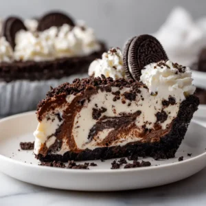 A decadent slice of creamy no-bake Oreo pie on a white plate, showing the distinct layers of Oreo cookie crust and cookies and cream filling.