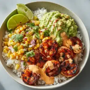 A close-up, overhead angle of a loaded healthy food bowl. Plump charred grilled shrimp, light green avocado mash, bright yellow corn salsa, and pale orange spicy-lime dressing.