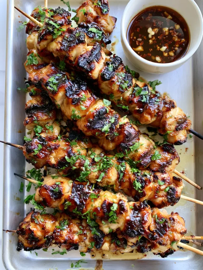 Honey Garlic Chicken Skewers: The Ultimate Charred & Glazed Summer Recipe 1 Detailed shot of charred chicken breast cubes with honey garlic glaze and minced garlic bits on an aluminum sheet.