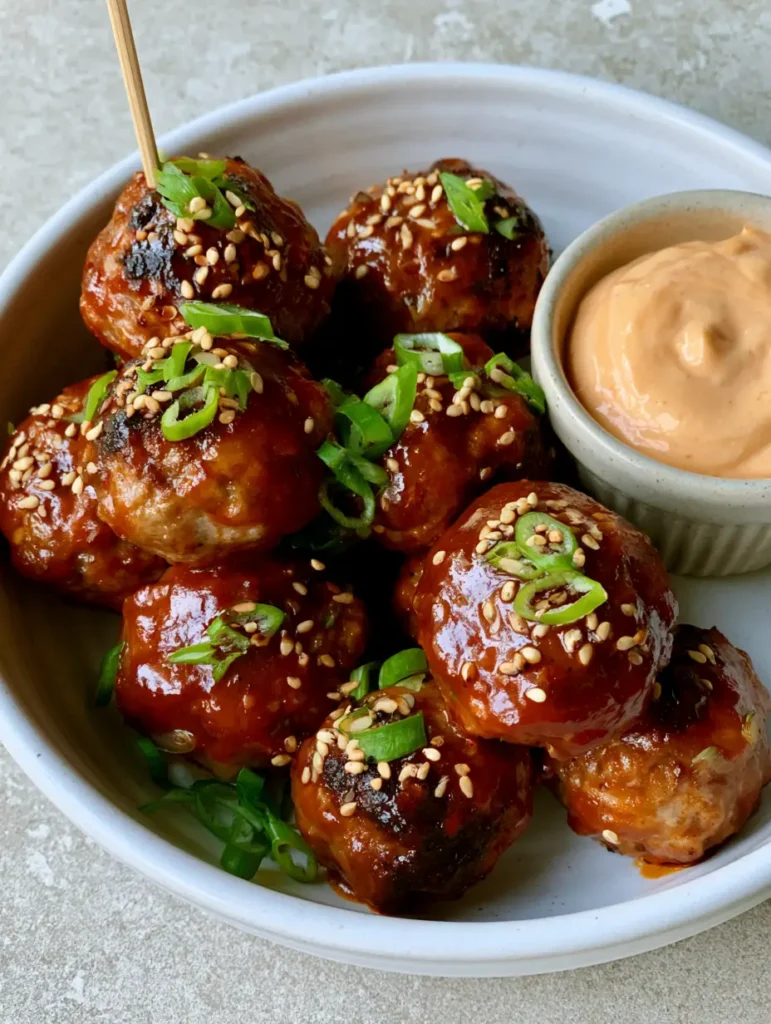 Korean BBQ Meatballs with a Thick Glossy Gochujang Glaze 1 Close-up of glazed Korean BBQ Meatballs topped with fresh green scallions and toasted white sesame seeds on a grey stone background.
