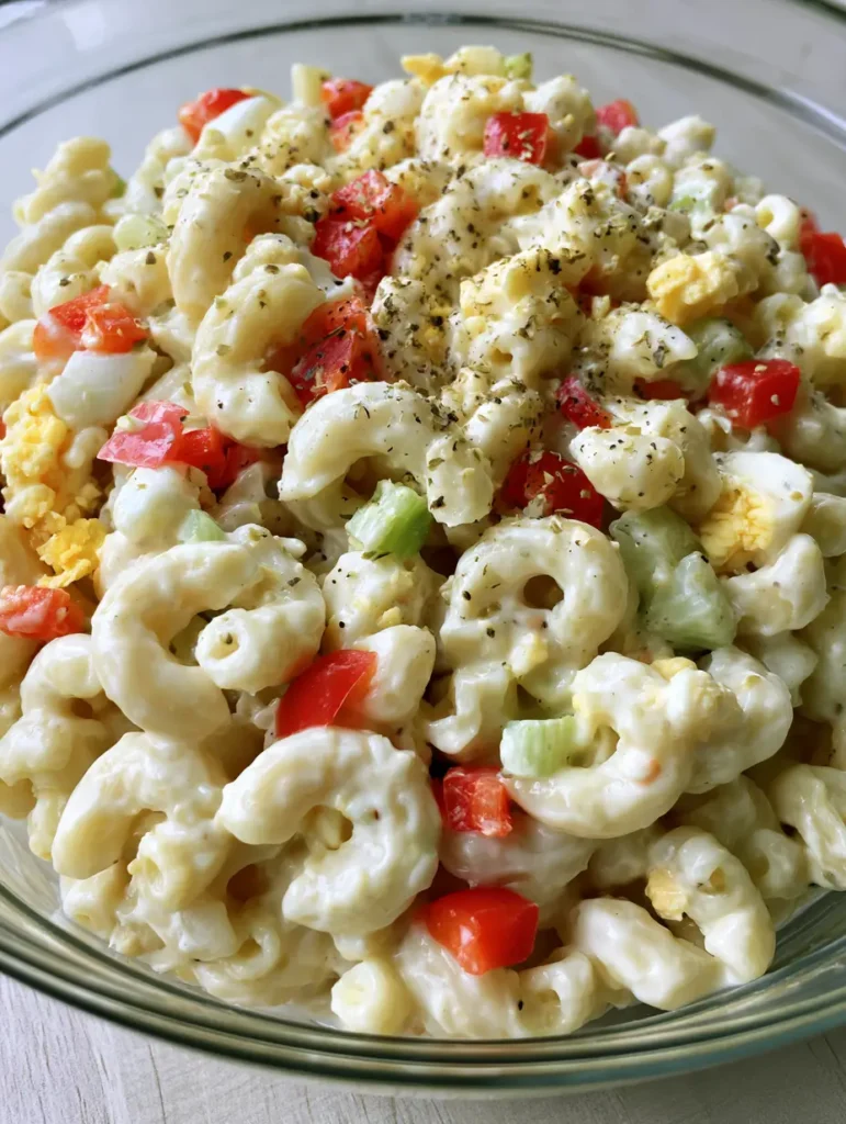 Amish Pasta Salad: The Ultimate Creamy and Tangy Summer Classic 1 High-angle view of Amish Pasta Salad in a clear glass bowl on a wooden surface.