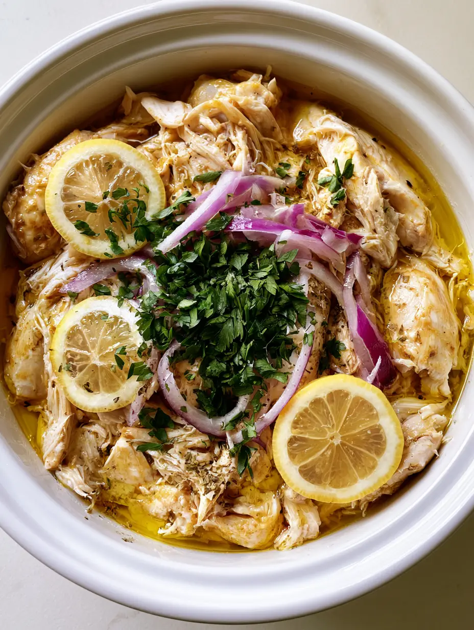 Slow Cooker Greek Chicken with Lemon and Oregano 4 Close up view of glistening shredded chicken breast in golden juices for Slow Cooker Greek Chicken recipe.